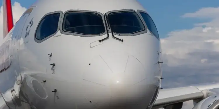 Primer plano de la cabina y el morro de un avión comercial moderno contra un cielo azul con nubes.