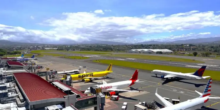 Vista aérea de varios aviones comerciales de diferentes aerolíneas estacionados en las puertas de embarque de un aeropuerto bajo un cielo nublado.