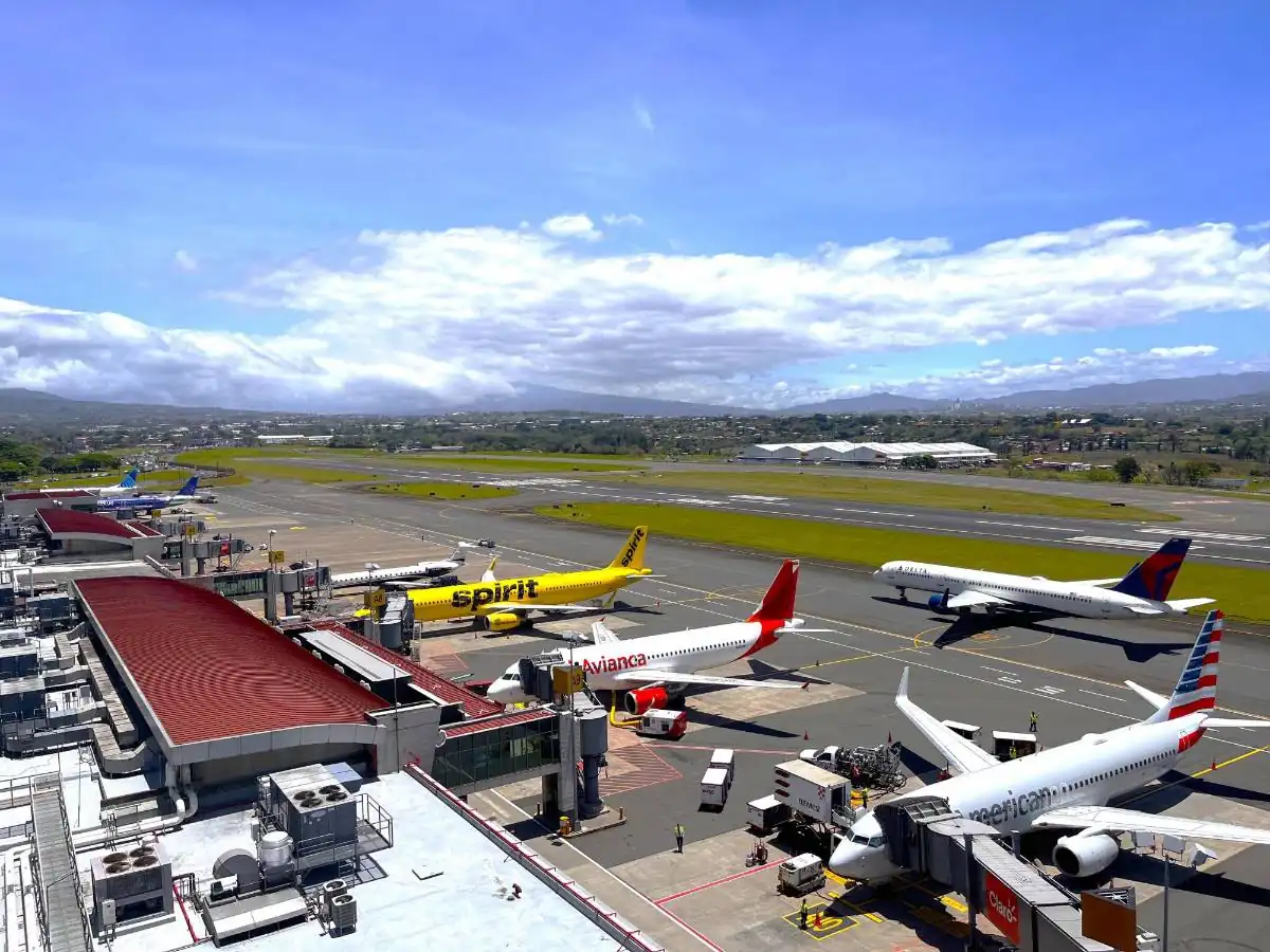 Vista aérea de varios aviones comerciales de diferentes aerolíneas estacionados en las puertas de embarque de un aeropuerto bajo un cielo nublado.