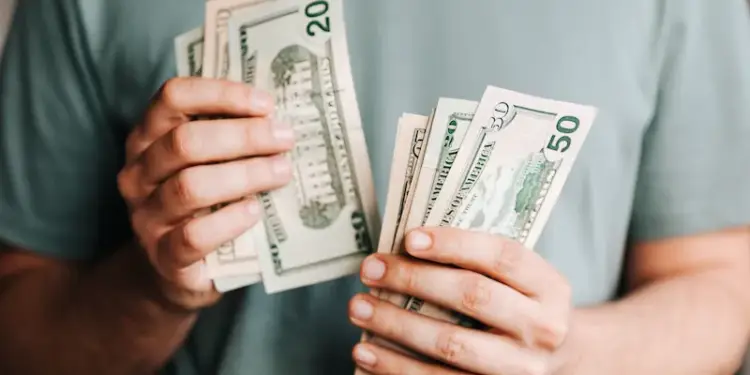 Primer plano de manos contando y sosteniendo billetes de dólares estadounidenses de veinte y cincuenta.
