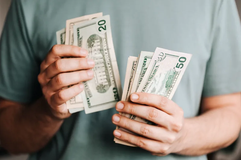 Primer plano de manos contando y sosteniendo billetes de dólares estadounidenses de veinte y cincuenta.