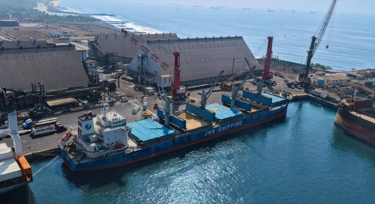 Vista aérea de un gran buque carguero atracado en un puerto industrial con grúas y grandes almacenes junto al mar.