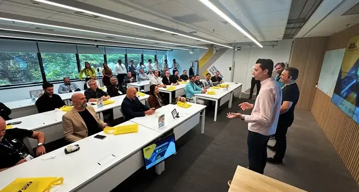 Un expositor habla ante un grupo de ejecutivos y profesionales sentados en una moderna sala de reuniones corporativas.