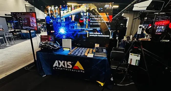 Stand corporativo con pantallas, cámaras de seguridad y una mesa cubierta con un mantel azul de Axis Communications.