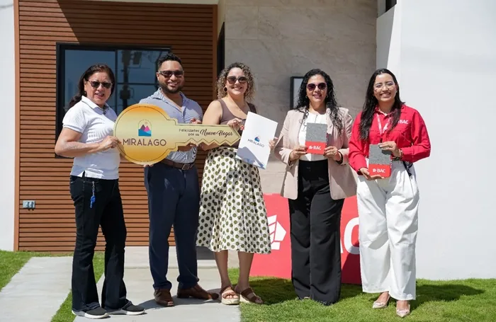 Cinco personas, tres mujeres y dos hombres, celebran la entrega de una vivienda. Sostienen una llave gigante de 'MIRALAGO' y documentos de 'BAC'.