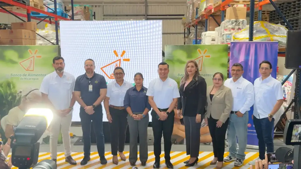 Grupo de nueve profesionales posando juntos en un almacén frente a una pantalla y banners corporativos.
