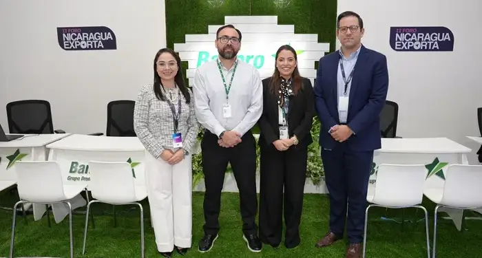 Cuatro profesionales de negocios de pie en un evento corporativo frente a un panel decorativo.
