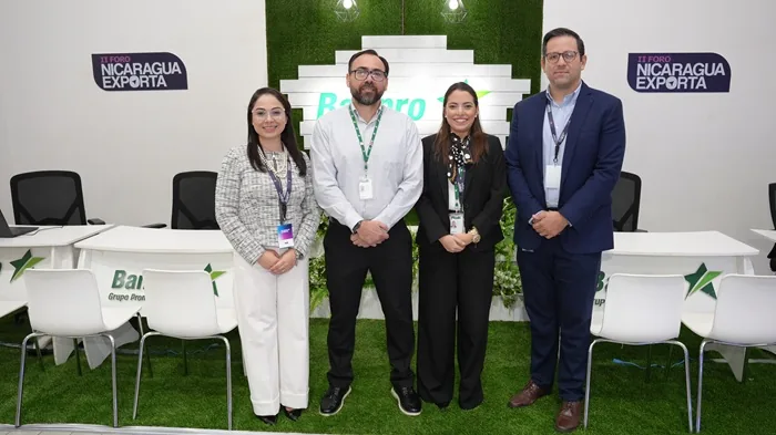 Cuatro profesionales de negocios de pie en un evento corporativo frente a un panel decorativo.