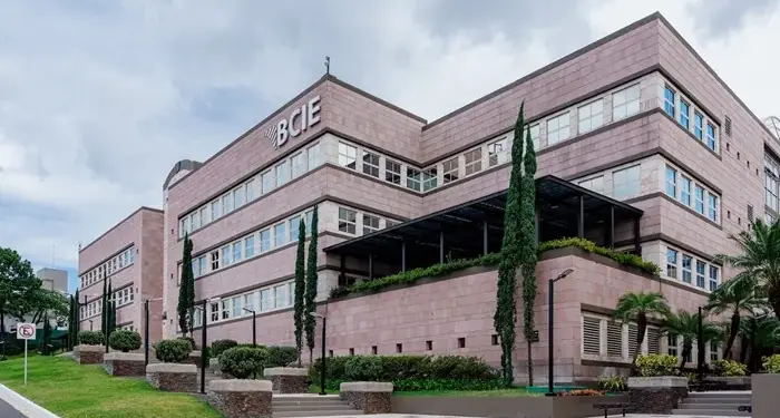 Vista exterior del edificio institucional del BCIE con fachada de bloques rosados y árboles altos.