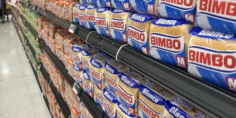 Un pasillo de supermercado con estantes repletos de paquetes de pan blanco y de trigo, mostrando la variedad de productos disponibles para el consumidor.