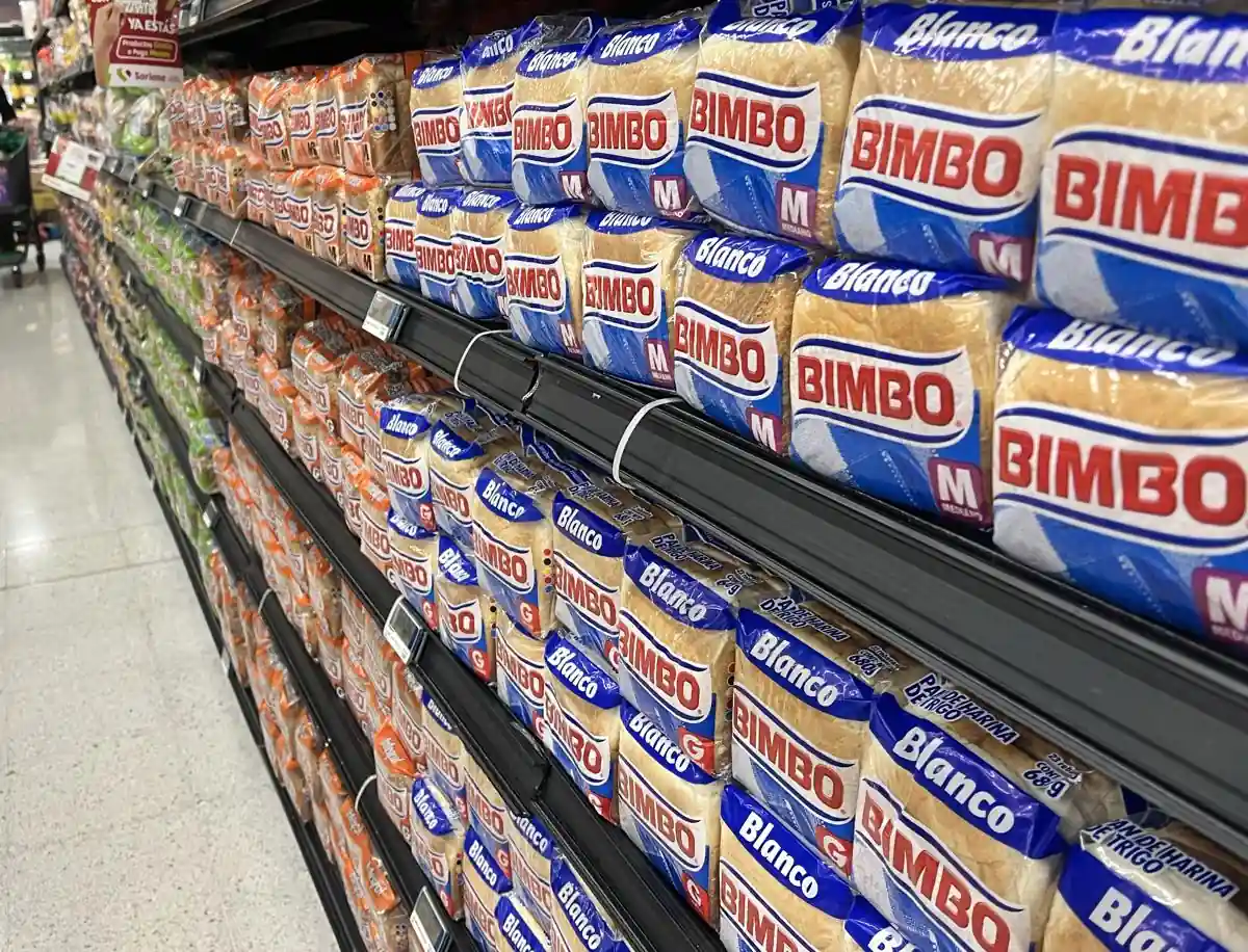 Un pasillo de supermercado con estantes repletos de paquetes de pan blanco y de trigo, mostrando la variedad de productos disponibles para el consumidor.
