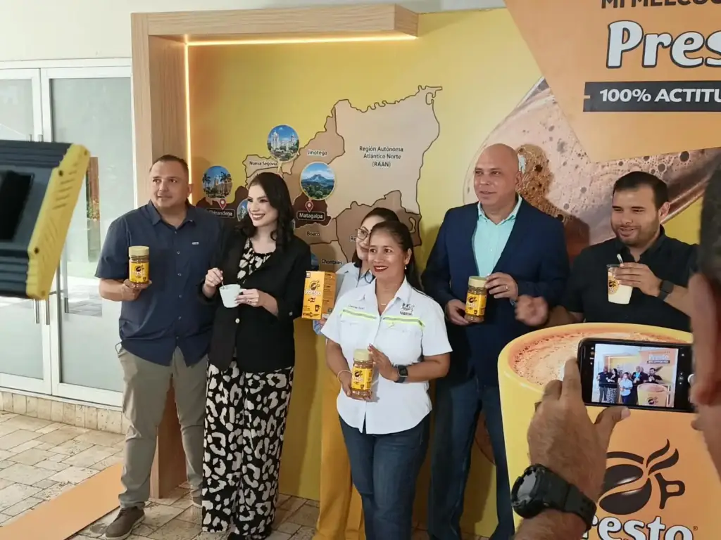 Ejecutivos y colaboradores sostienen frascos de Café Presto frente a un mapa de Nicaragua durante el lanzamiento de la campaña Mi Melcochita