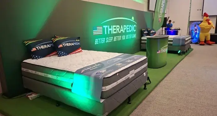 Stand comercial con colchones de la marca Therapedic expuestos en un evento corporativo con iluminación verde.