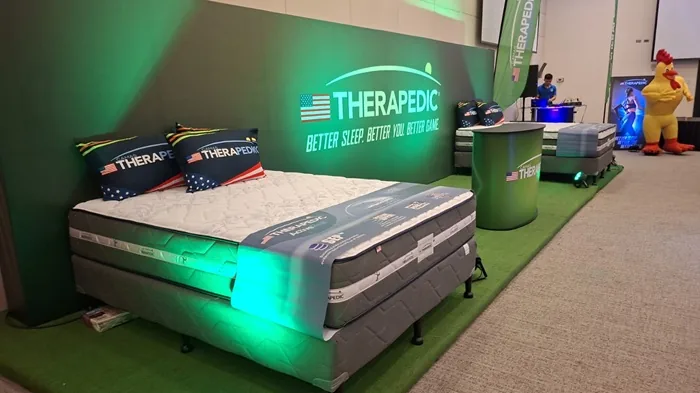 Stand comercial con colchones de la marca Therapedic expuestos en un evento corporativo con iluminación verde.