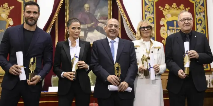 Grupo de cinco personas de pie sosteniendo diplomas y estatuillas doradas en un evento institucional formal.
