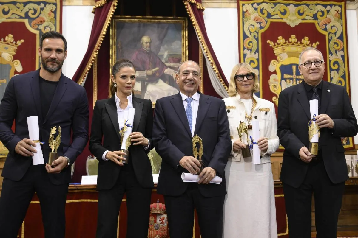 Grupo de cinco personas de pie sosteniendo diplomas y estatuillas doradas en un evento institucional formal.