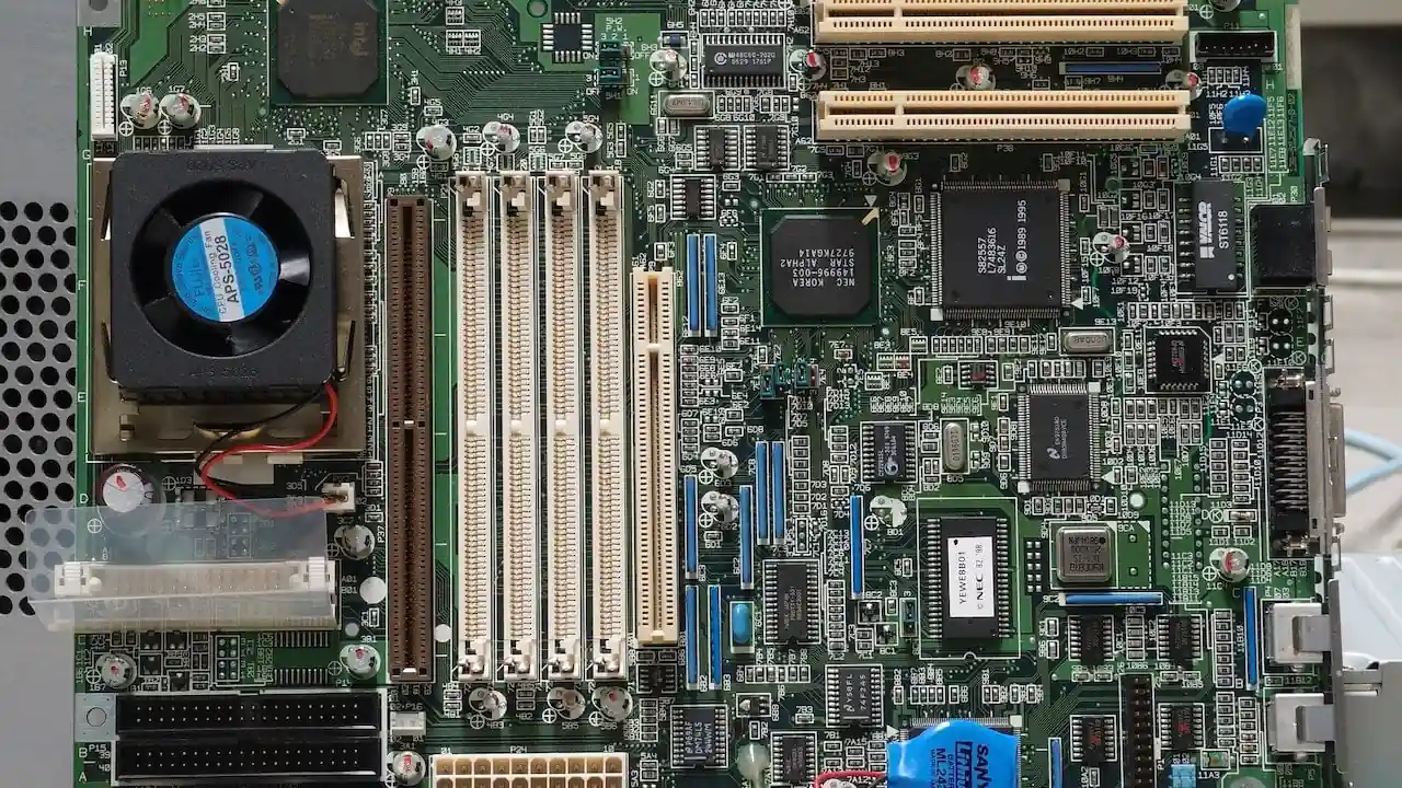 Vista superior de una placa base verde con un ventilador, chips, condensadores y múltiples ranuras de expansión.