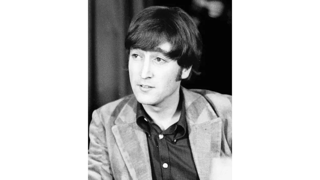 Fotografía en blanco y negro de un hombre con cabello oscuro y flequillo, vestido con chaqueta y camisa oscura.