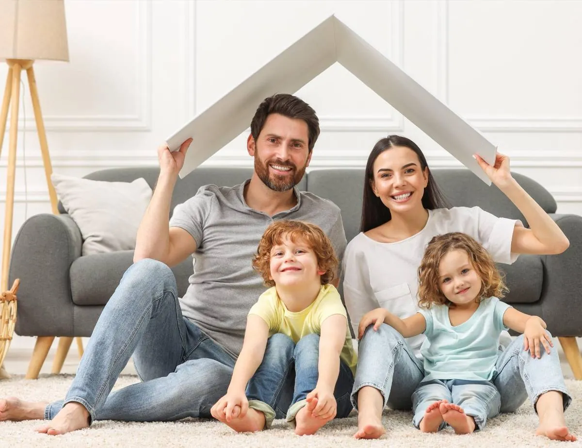 Familia sonriente sosteniendo un tejado de cartón simulando una casa en la sala de estar