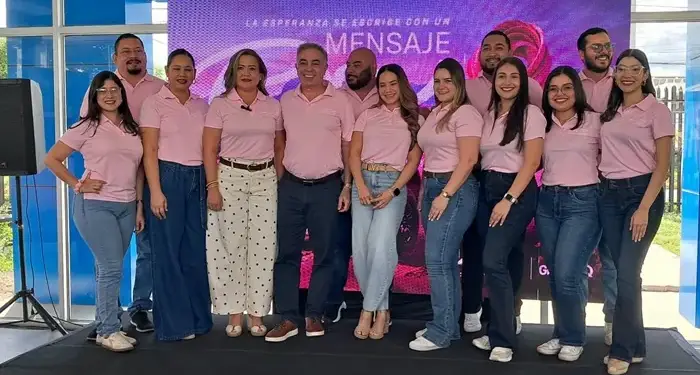 Grupo de hombres y mujeres profesionales vestidos con camisas rosadas y jeans en un evento empresarial.