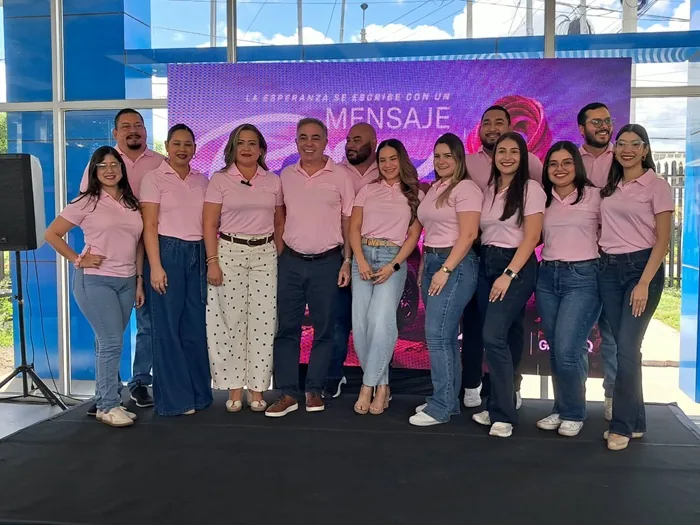 Grupo de hombres y mujeres profesionales vestidos con camisas rosadas y jeans en un evento empresarial.