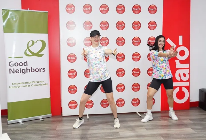 Dos mujeres bailando y haciendo ejercicio frente a un panel con logotipos de marcas corporativas en un evento.