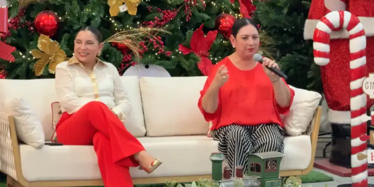Dos mujeres sentadas en un sofá blanco conversando en un evento corporativo navideño con decoración festiva de fondo.