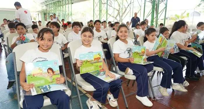 Grupo de niños y niñas sentados en sillas sosteniendo cuadernos ilustrados en una actividad escolar.