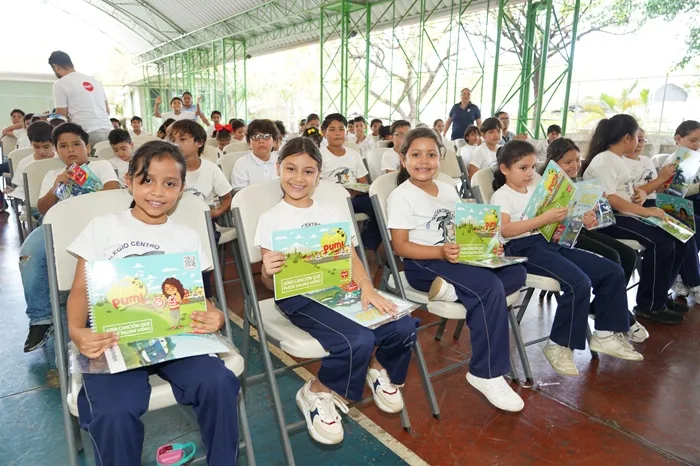 Grupo de niños y niñas sentados en sillas sosteniendo cuadernos ilustrados en una actividad escolar.