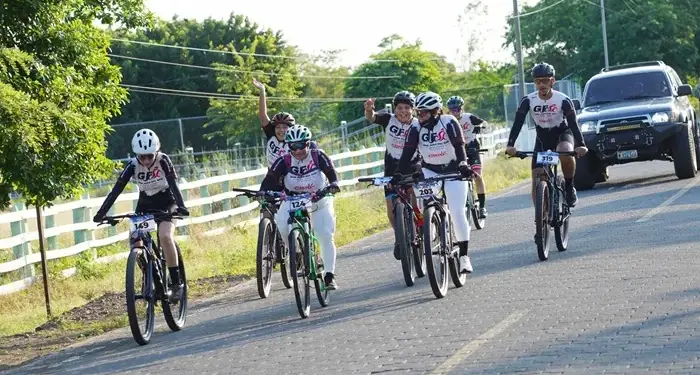 Grupo de personas con equipo deportivo y cascos montando bicicletas en una carretera pavimentada rodeada de vegetación.