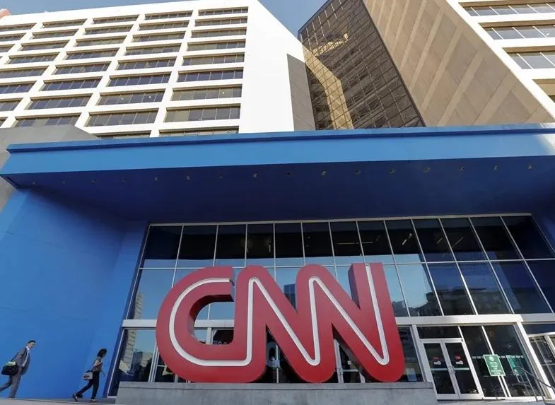 Fachada de un edificio corporativo moderno con el logotipo rojo de CNN en la entrada principal y personas caminando.