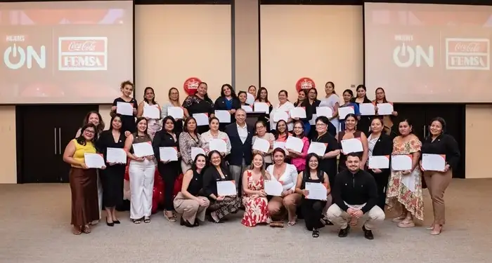 Amplio grupo de mujeres y algunos hombres posando con diplomas en un evento corporativo de Coca-Cola FEMSA.