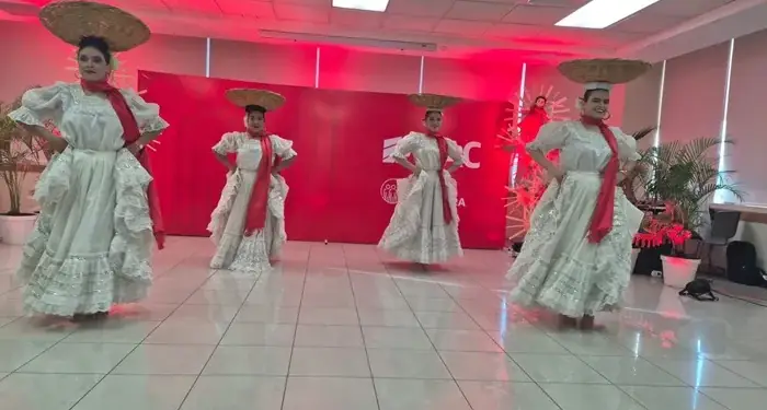Cuatro mujeres con trajes tradicionales blancos y sombreros bailando en un salón corporativo con iluminación roja de fondo.