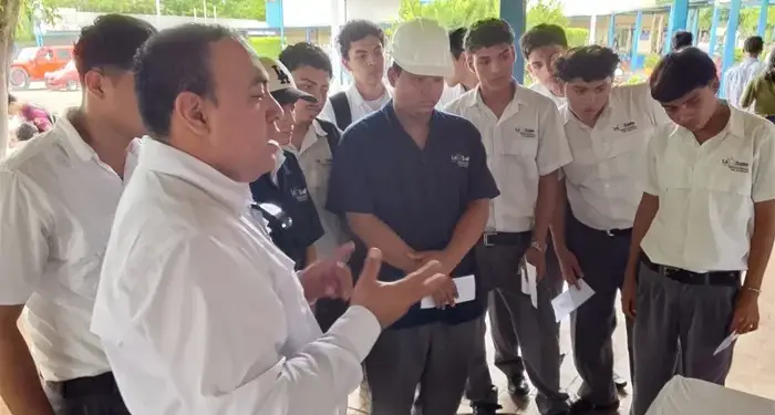 Un instructor explicando a un grupo de jóvenes estudiantes varones en un espacio al aire libre.