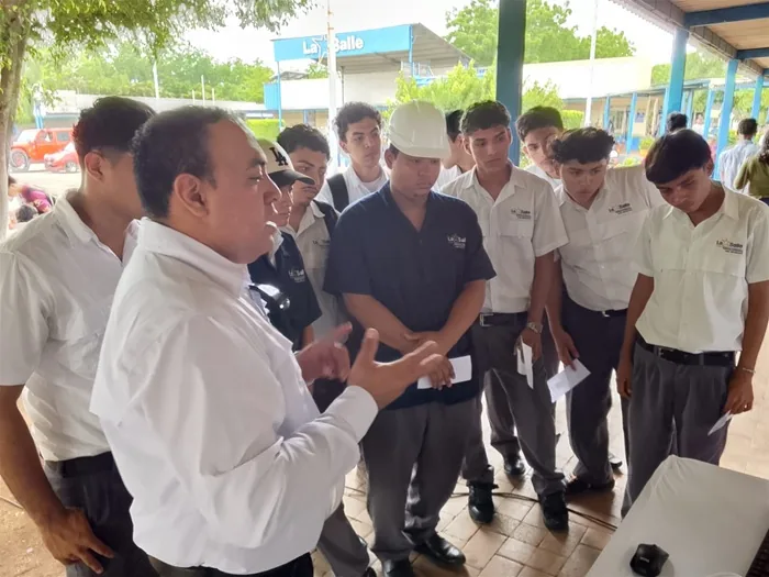 Un instructor explicando a un grupo de jóvenes estudiantes varones en un espacio al aire libre.