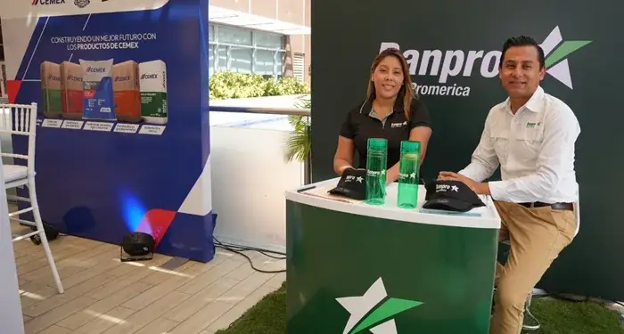 Dos personas sonriendo junto a un mostrador corporativo con logotipos de Banpro Promerica y Cemex en un evento