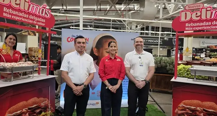 Tres profesionales de pie junto a estands promocionales en el pasillo de un supermercado.