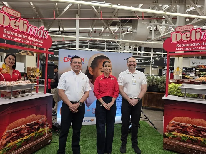 Tres profesionales de pie junto a estands promocionales en el pasillo de un supermercado.