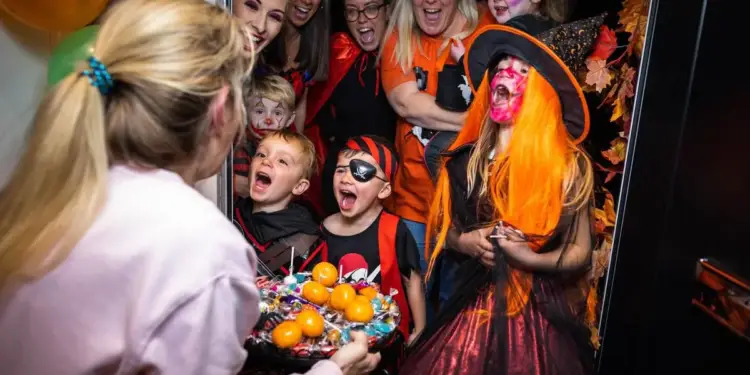 Grupo de niños y adultos disfrazados celebrando la fiesta de Halloween en una puerta.