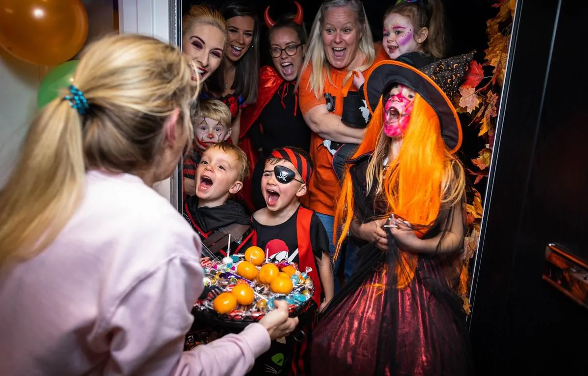Grupo de niños y adultos disfrazados celebrando la fiesta de Halloween en una puerta.