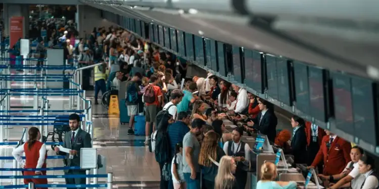 Pasajeros y personal en un aeropuerto concurrido, haciendo fila en mostradores de check-in. Muestra la actividad del transporte aéreo.