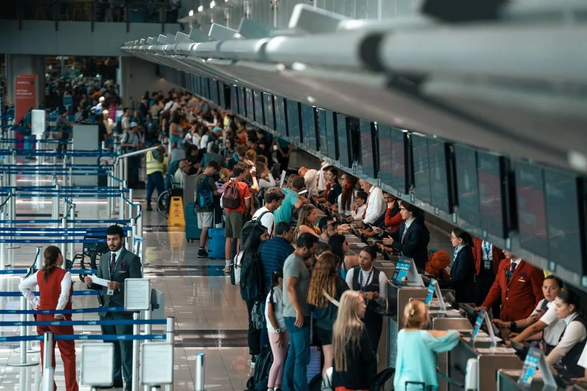 Pasajeros y personal en un aeropuerto concurrido, haciendo fila en mostradores de check-in. Muestra la actividad del transporte aéreo.