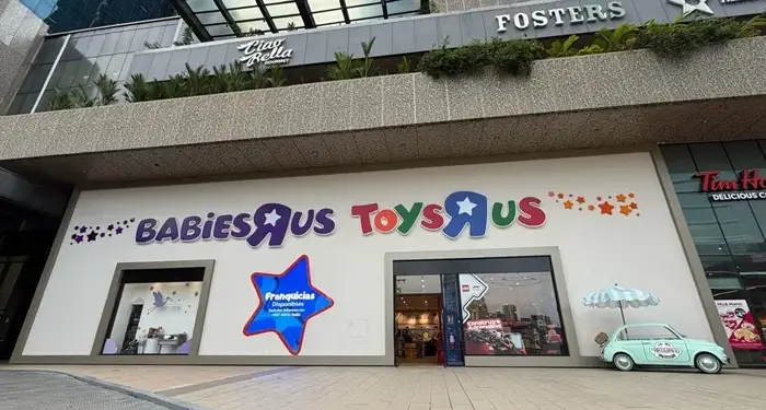 Fachada de tiendas "Babies R Us" y "Toys R Us" en un centro comercial, con un pequeño coche decorativo y un cartel de "Franquicias Disponibles".