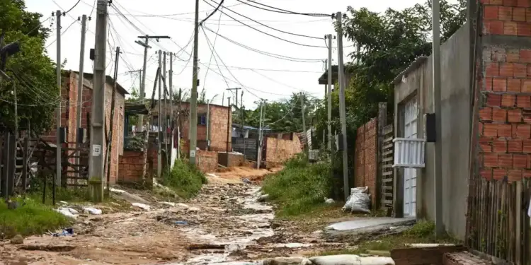 Calle de tierra y barro con cables eléctricos entrelazados y casas de ladrillo en zona de bajos recursos