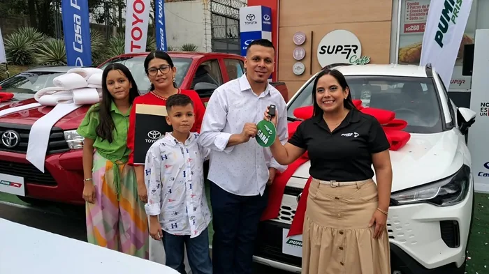 Familia recibiendo las llaves de un automóvil nuevo decorado con un moño rojo junto a un asesor comercial en un concesionario.