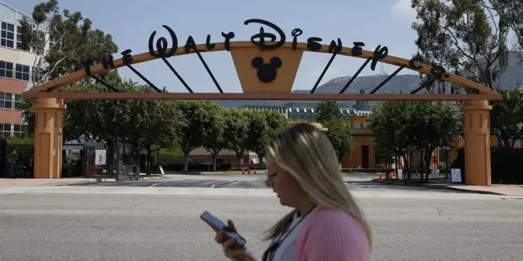 Mujer usando un teléfono móvil frente a la entrada principal con el letrero de The Walt Disney Co.