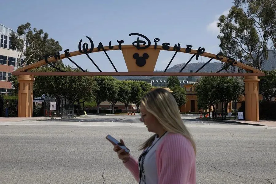 Mujer usando un teléfono móvil frente a la entrada principal con el letrero de The Walt Disney Co.