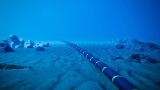 Cable submarino negro con franjas amarillas extendiéndose por el fondo marino de arena en aguas azules.