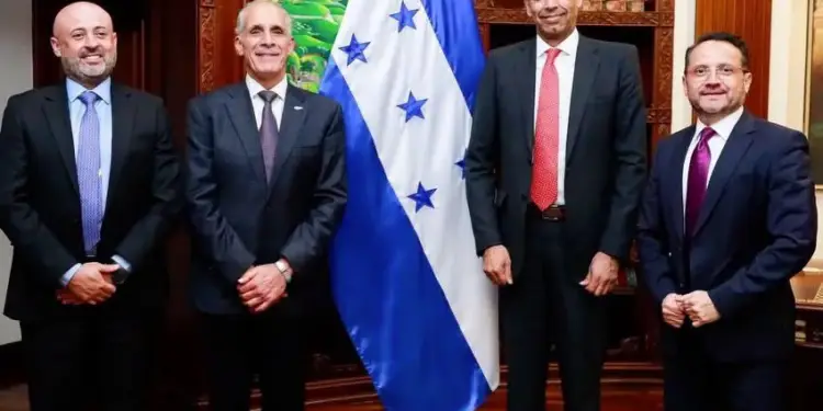 Cuatro hombres con traje formal posan de pie frente a la bandera de Honduras en una oficina.
