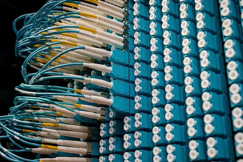 Panel con conectores de fibra óptica y cables azules conectados en un servidor de datos.